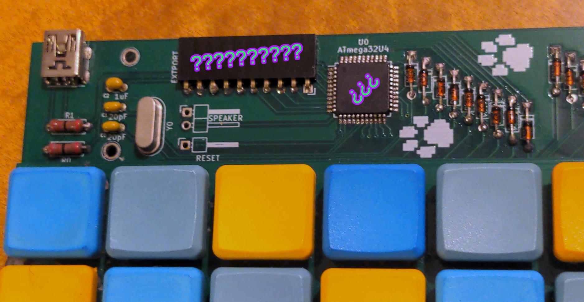 A close up to the keyboard's upper left corner; electronic chips and components are shown; colorful question marks are overlaid above two components that look like black rectangles.