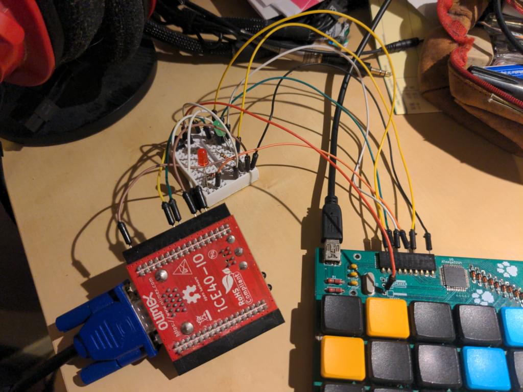 The keyboard's extension port wired to a breadboard with two LEDs and a button, wired to a red Olimex PCB that features a VGA connector.